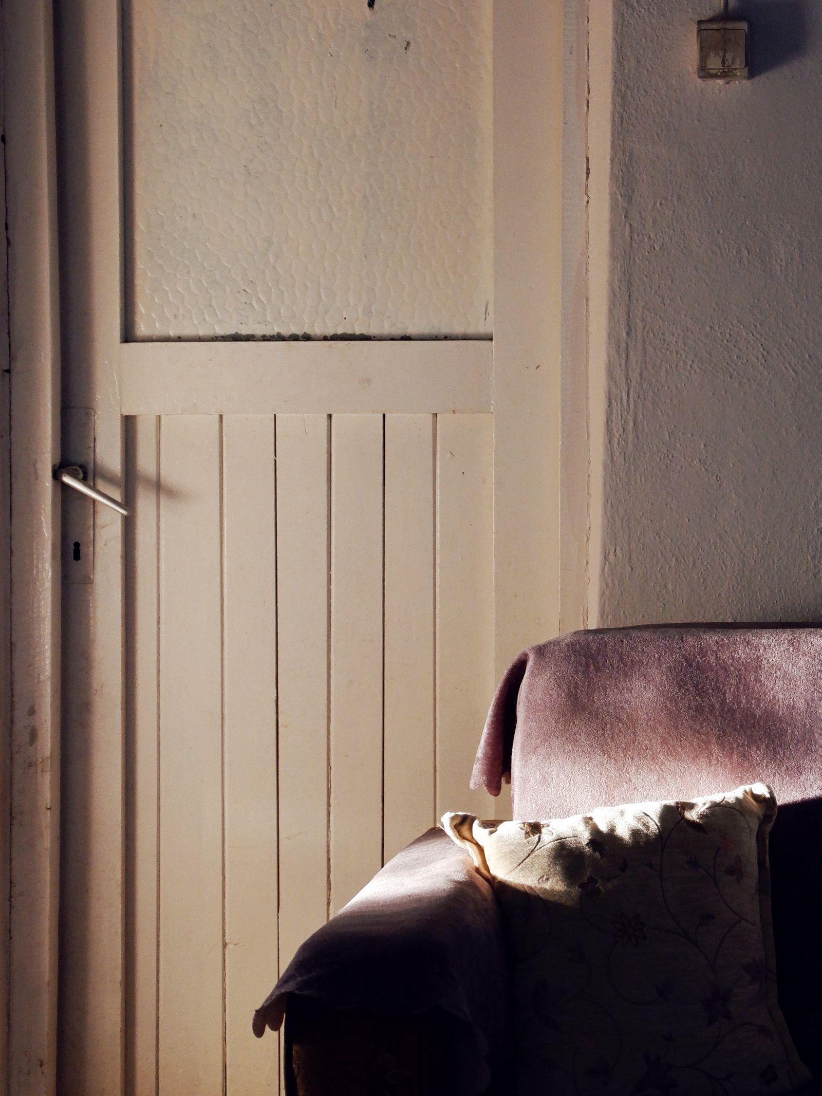A quiet sunlit corner of a home, with an armchair by a wooden door